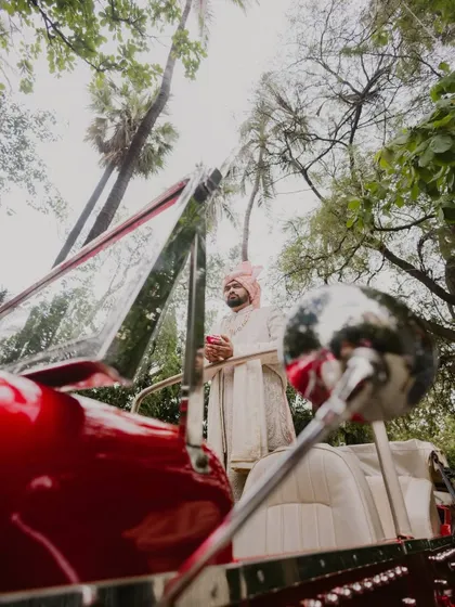 The groom's grand entrance in a vintage car at a lush, green wedding venue. This shot captures the style and excitement of a destination wedding baraat.