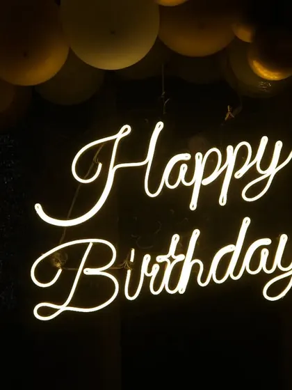A detailed shot of the "Happy Birthday" neon sign, a popular decoration for modern parties. We focus on capturing the mood and ambiance.