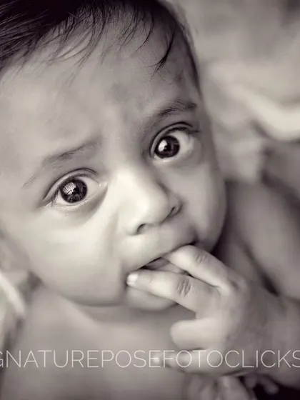 A black and white portrait capturing a newborn's curious expression and tiny fingers exploring their mouth.