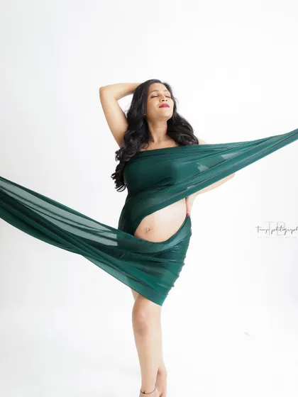 A modern and artistic portrait. The mom-to-be is wrapped in flowing green fabric, creating a dynamic and stylish image.
