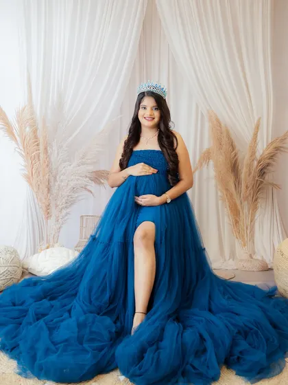 A duplicate of image 180, this portrait features a mom-to-be in a voluminous blue gown and tiara, seated in a boho-chic setting.