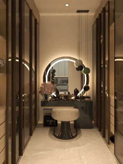 A glamorous walk-in closet with a dedicated makeup vanity at the end. The circular back-lit mirror and glass wardrobe doors create a bright and stylish space.
