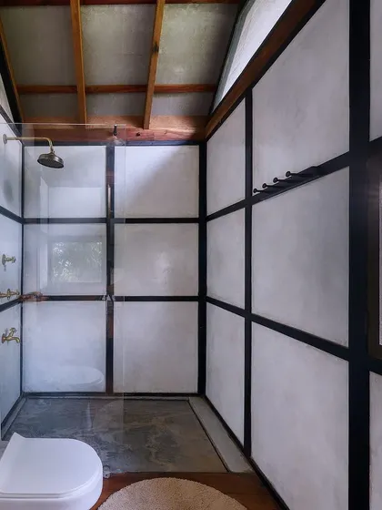 The walk-in shower area, with lime-plastered walls and exposed wooden framing. The design is minimalist yet warm, with a window that brings in natural light and a connection to the outdoors.