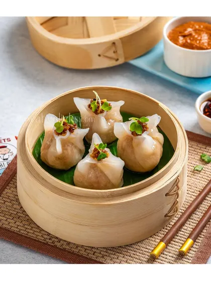 Steamed chicken dim sum in a bamboo basket, garnished with microgreens.