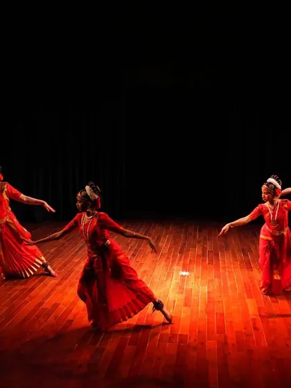 A wide shot of my students performing on stage. The rich red costumes and the stark black background create a powerful visual contrast, typical of classical dance productions.