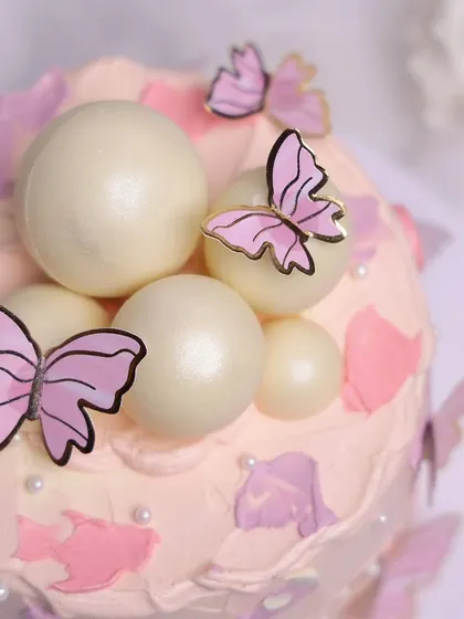 We create a magical garden with this pink butterfly cake. A flurry of pink and gold butterflies appears to dance around the cake, which is decorated with abstract pink frosting and shimmering white chocolate spheres, perfect for a whimsical birthday.
