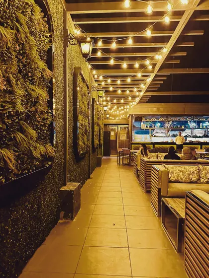 I designed this rooftop cafe to be an inviting evening destination. The combination of a full-length vertical garden, warm string lights under a pergola, and comfortable slatted wood seating creates a cozy and vibrant ambiance for guests.