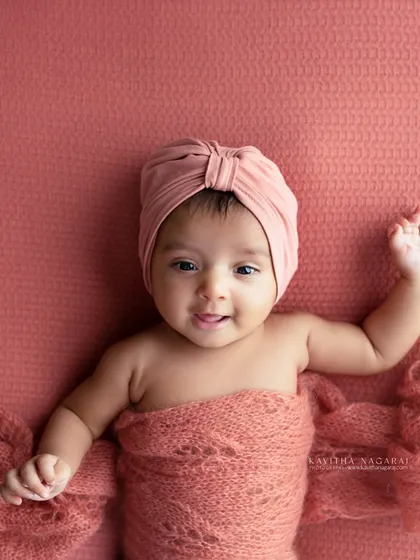 Another angle of an older newborn, showing off their happy expression. The warm, peachy tones of the wrap and background create a joyful and inviting image.