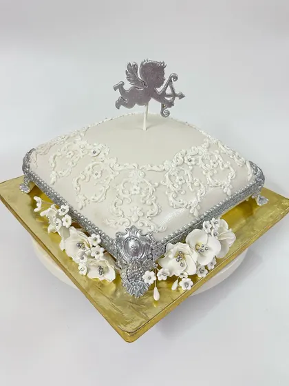 The full view of the angel-themed cake, designed to look like a royal cushion. The silver accents and white sugar flowers add to its heavenly appearance.