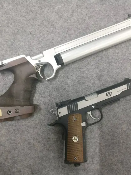 A competition air pistol and a .22 caliber Colt pistol side by side. We offer training in various categories, from the 10m air pistol Olympic event to other firearm shooting experiences.