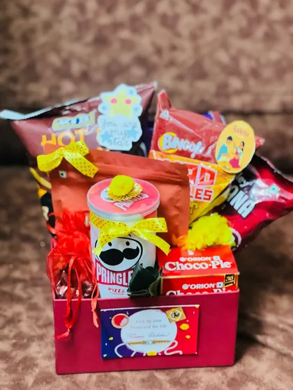 A fun and snack-filled Rakhi hamper for someone who loves munchies, featuring Pringles, Bingo, and Choco-Pie in a bright red box.