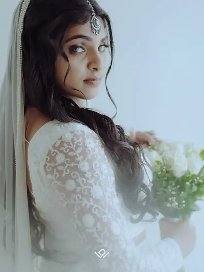 A soft, dreamy portrait of a bride in a white lace lehenga, holding a bouquet of white roses, perfect for a Nikah or reception.