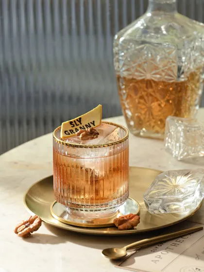A classic old-fashioned style cocktail, the Name Dropper, served in a crystal-cut glass with a large ice cube and garnished with a walnut.