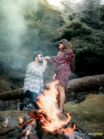 A romantic proposal scene by a bonfire in the woods, with smoke adding a mystical effect to this intimate pre-wedding moment.