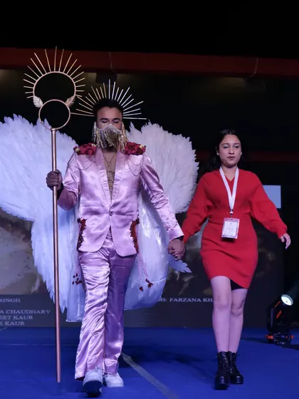 A student designer and his model present a fantasy-inspired pink suit with angel wings and a staff.