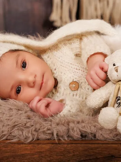 Wide awake and curious, this newborn cuddles with a teddy bear in a rustic wooden bed prop, showing that awake shots can be just as precious.