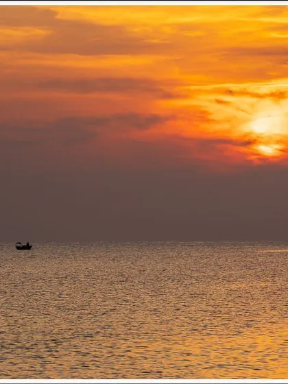 A lone fishing boat sails on the calm sea under a fiery sunset in the Andaman Islands. This is a simple, minimalist composition that evokes a sense of peace.
