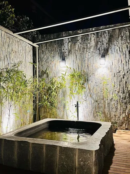 The bath is set on a wooden deck and enclosed by textured stone walls and bamboo plants to create a private, Zen-like retreat.