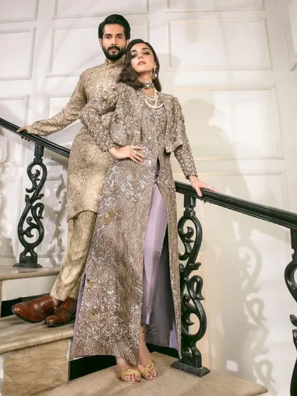 This is a great example of modern coordination. Her outfit features a long, embroidered jacket over pants, and his sherwani uses the same fabric and embroidery in a more traditional silhouette.