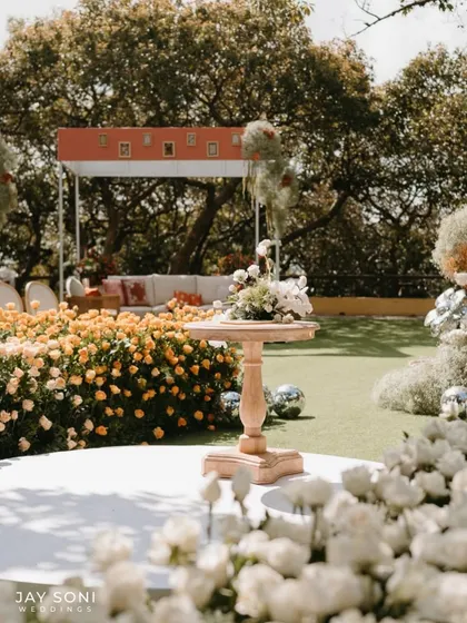 The wedding stage is set amidst a field of yellow and white roses, with modern lounge seating in the background, creating a beautiful blend of classic romance and contemporary style.