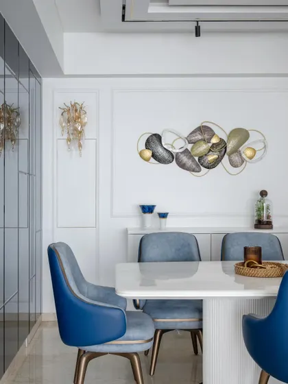 The dining area in this coastal-themed home features a striking metal wall sculpture and elegant wall sconces. The white and blue color scheme creates a serene and sophisticated atmosphere.