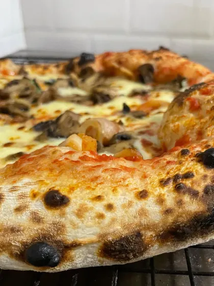 A side view of the Funghi pizza, highlighting the incredible oven spring and the airy, open structure of the cornicione, or crust.
