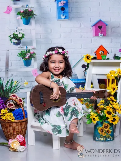 A little musician strumming her guitar in a bright and cheerful garden setting. The sunflowers, birdhouses, and her happy smile create a wonderfully sunny photo.
