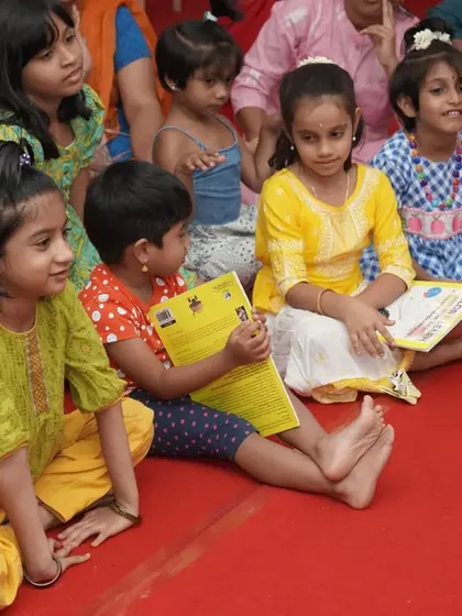 Young children sitting on the floor, holding their activity books and listening with rapt attention. This is the foundation of creating a lifelong audience for Indian art music.