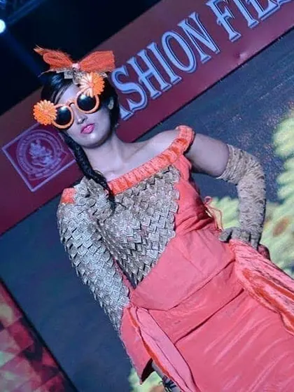 This runway look highlights creative accessorizing and fabric texturing. The student designer created a woven bodice and paired it with a flowing orange skirt and custom-made, whimsical sunglasses.