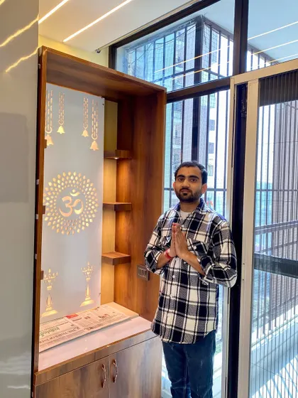 Standing with a completed mandir unit. This wooden design features a backlit acrylic panel with religious motifs and storage cabinets below.