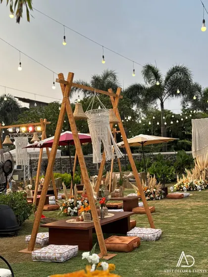 A charming low seating arrangement with a wooden A-frame structure, floor cushions, and a hanging macrame chandelier, perfect for a relaxed Mehendi or sundowner.