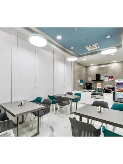 A dedicated cafe and refreshment area provides a comfortable space for patients and visitors. The design uses a mix of modern chairs, clean surfaces, and soft blue ceiling accents to create a relaxed and pleasant environment.