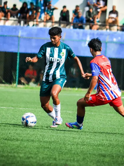 A player in our striped kit skillfully dribbles past an opponent, demonstrating the high level of technical ability in our youth leagues.