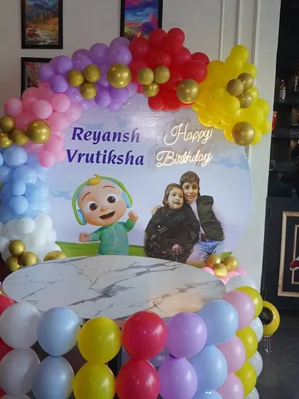 A Cocomelon themed birthday party with a cake table setup. The decoration features a custom backdrop, a balloon arch, and a balloon-wrapped table.