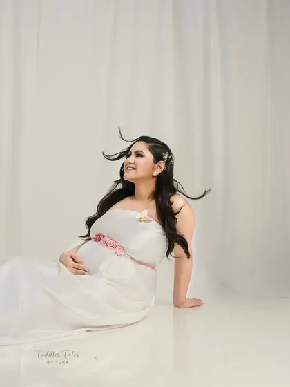 A portrait of pure joy. The wind in her hair and the soft white dress create a feeling of freedom and happiness. This is a celebration of the beautiful journey of motherhood.