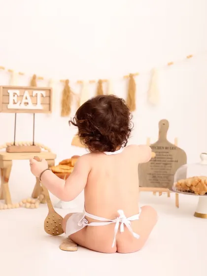 The cheeky side of the little chef! This playful shot from behind captures the adorable details of the setup and the baby's fun-loving spirit.