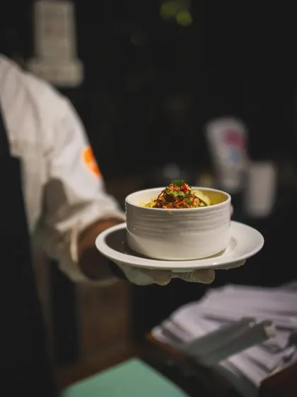 A chef carefully adds toppings to a freshly prepared bowl of Khow Suey at a live station.