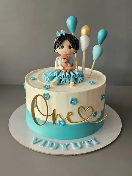 What was your favorite doll as a kid? This chocolate mousse cake for Vidyuti's first birthday features a cute girl in a teal dress holding her teddy bear.