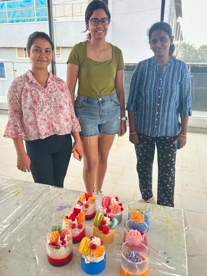 Three participants with their finished dessert candles, including intricate macaron and fruit designs.