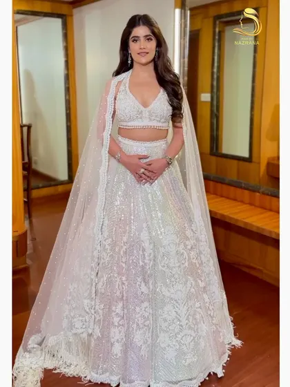 A full-length view of the bride-to-be in her stunning white lehenga, her soft curls adding a touch of glamour to the engagement look.