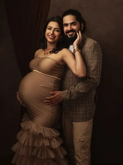 A glamorous fine art maternity portrait. The couple's joyful expression and the textured gown create a sophisticated and celebratory image against a classic studio backdrop.