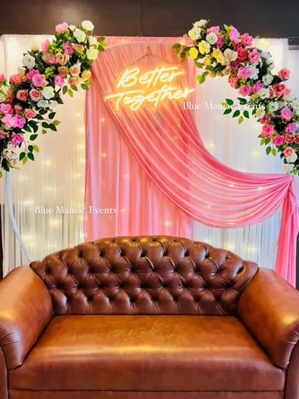 A lovely Roka backdrop with a circular frame, pink draping, and a pink and white floral arch. The tufted leather sofa adds a touch of classic comfort to the modern setup.