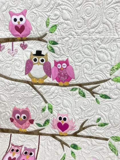 A close-up of the owl family quilt, showing the adorable appliqué details like a top hat and heart-shaped wings.