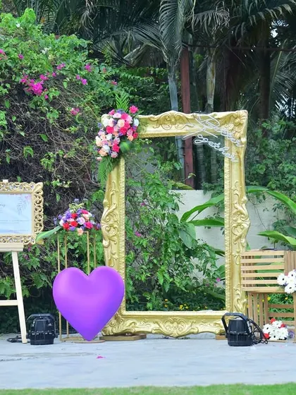 A wide view of the golden frame photo booth in a garden setting, complete with heart-shaped props.