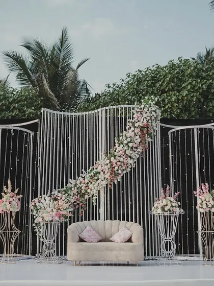 A modern and elegant reception stage. The clean lines of the white panelled backdrop are softened by asymmetrical cascades of pink and white flowers, creating a chic and sophisticated look.