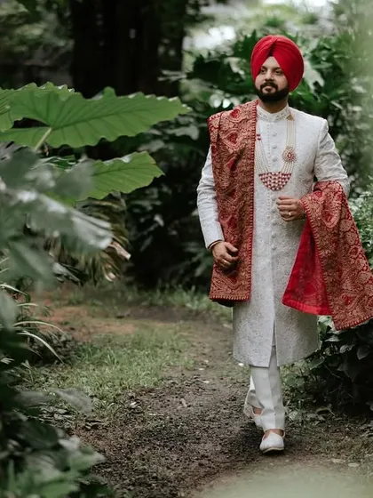 A candid portrait of the groom walking through a forest path. The framing with natural leaves adds depth and a sense of intimacy to the shot.