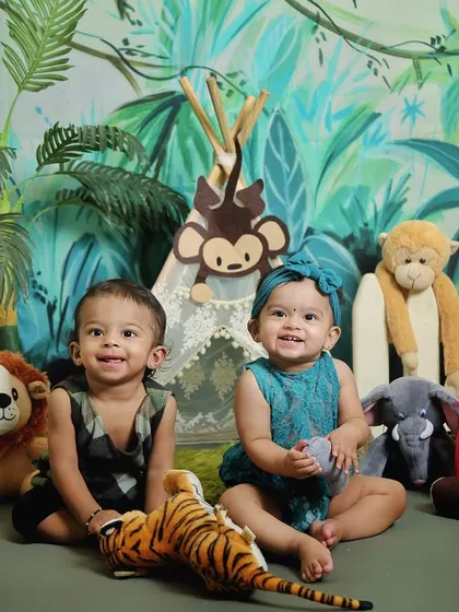 A brother and sister twin duo enjoying their jungle-themed photoshoot. The lush green backdrop and friendly animal props create a fun and wild setting.