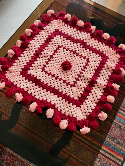 An angled shot of the festive pompom tablecloth, showing how it drapes over the corner of a glass table.