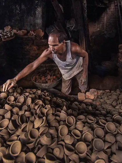 A potter carefully inspects a fresh batch of diyas, or clay lamps, before they are fired. The sheer volume of his craft fills the frame, showing the scale of production in this small workshop.