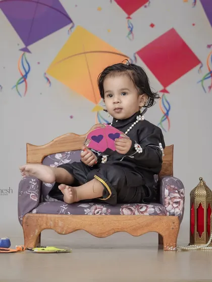 A thoughtful moment captured during the Makar Sankranti baby shoot. The black traditional outfit stands out against the light, festive background.
